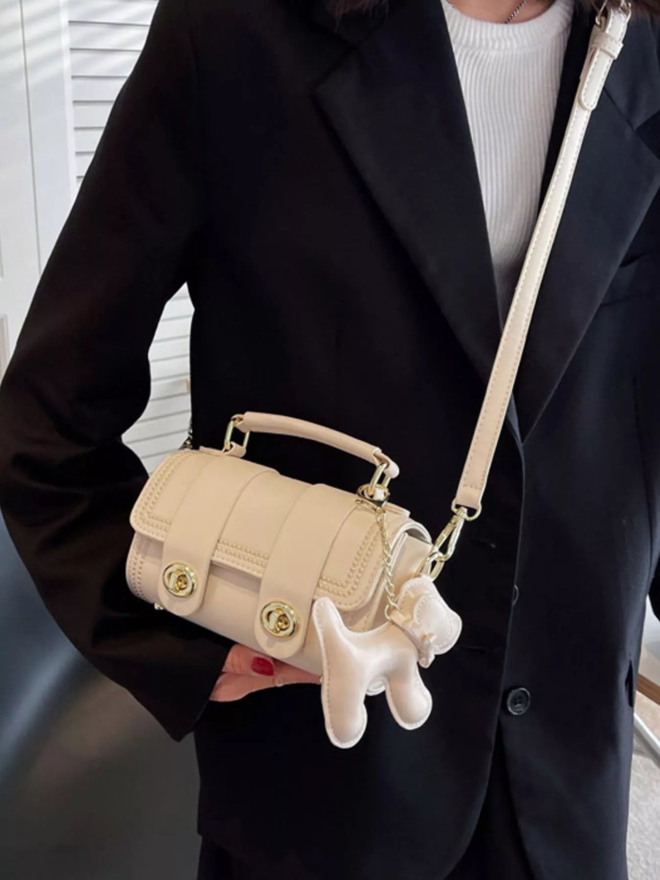 Person holding a beige handbag with a dog-shaped charm, wearing a black coat.