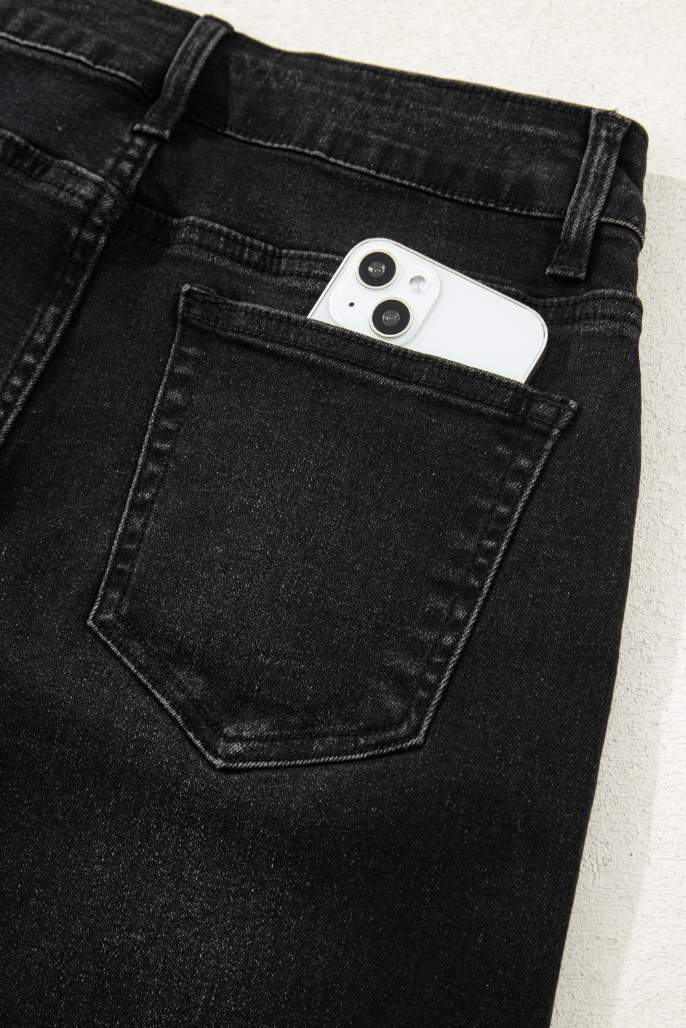 Black jeans with a smartphone in the pocket on a light background