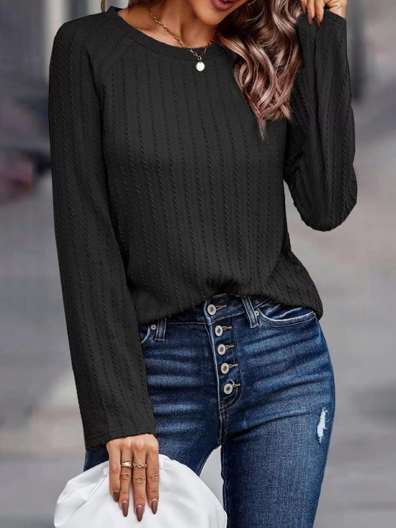 Person wearing a black long-sleeve top and blue jeans with a blurred background
