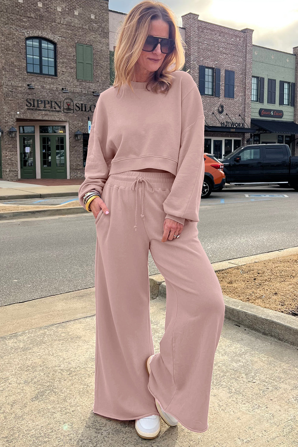Woman in a pink outfit standing on a sidewalk with a street and building in the background.