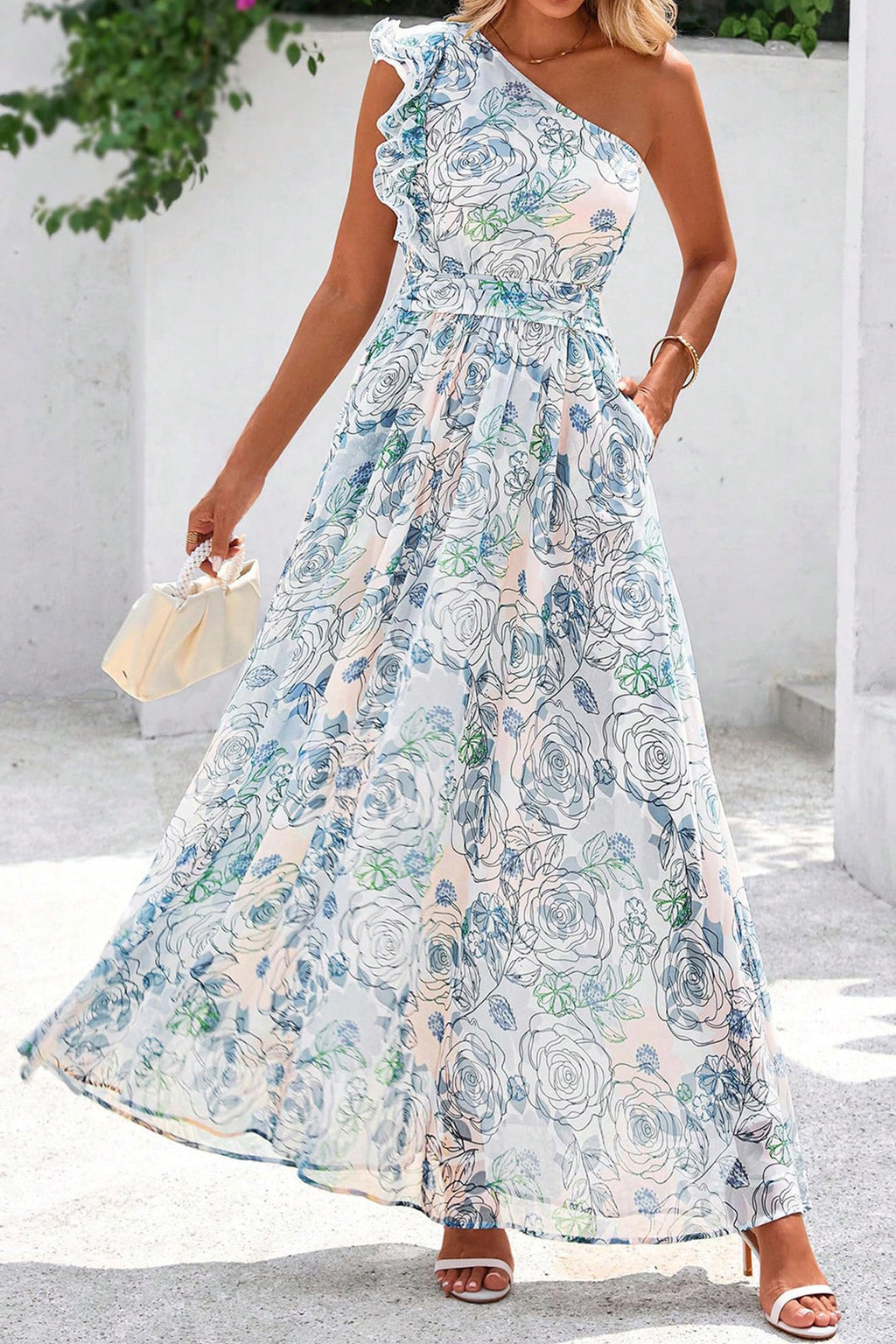 Woman wearing a floral one-shoulder dress against a white wall. Front view