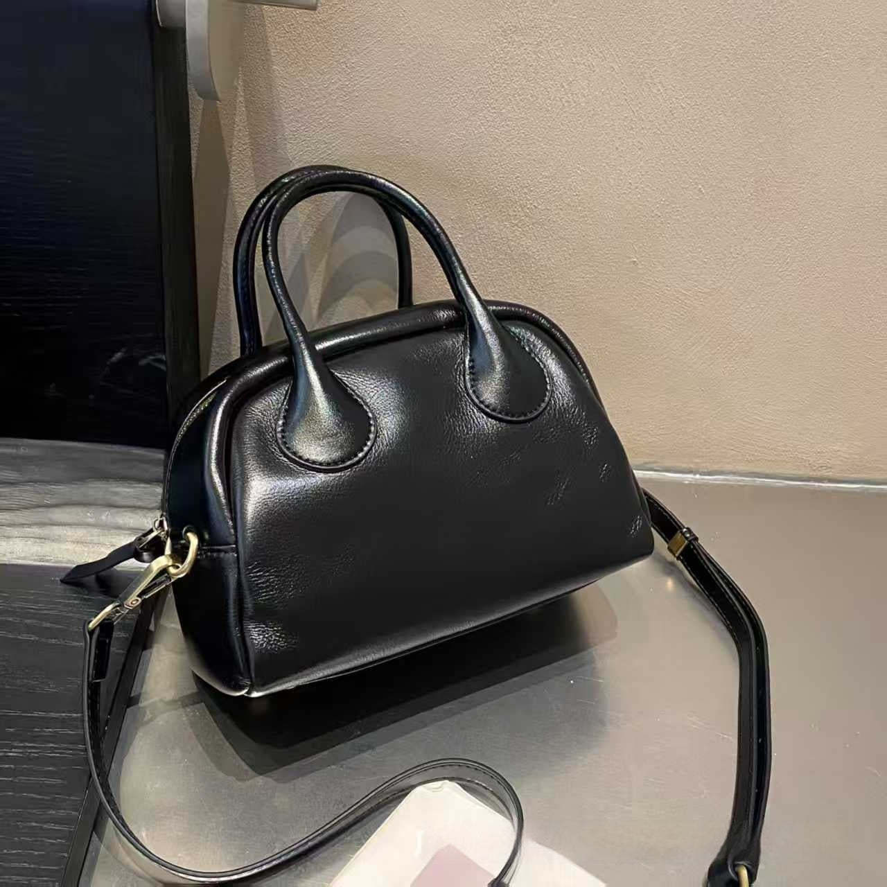Black handbag on a reflective surface with a neutral background