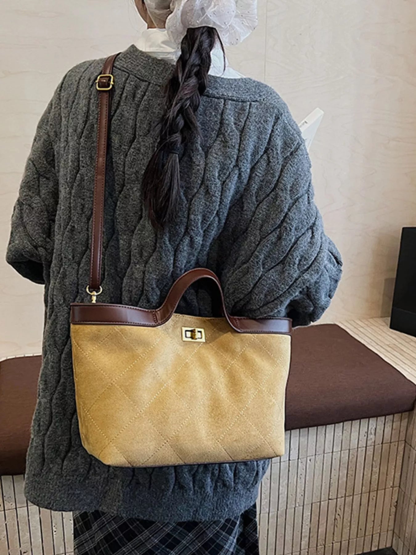 Person wearing a gray cable knit sweater and holding a beige handbag with a brown strap.