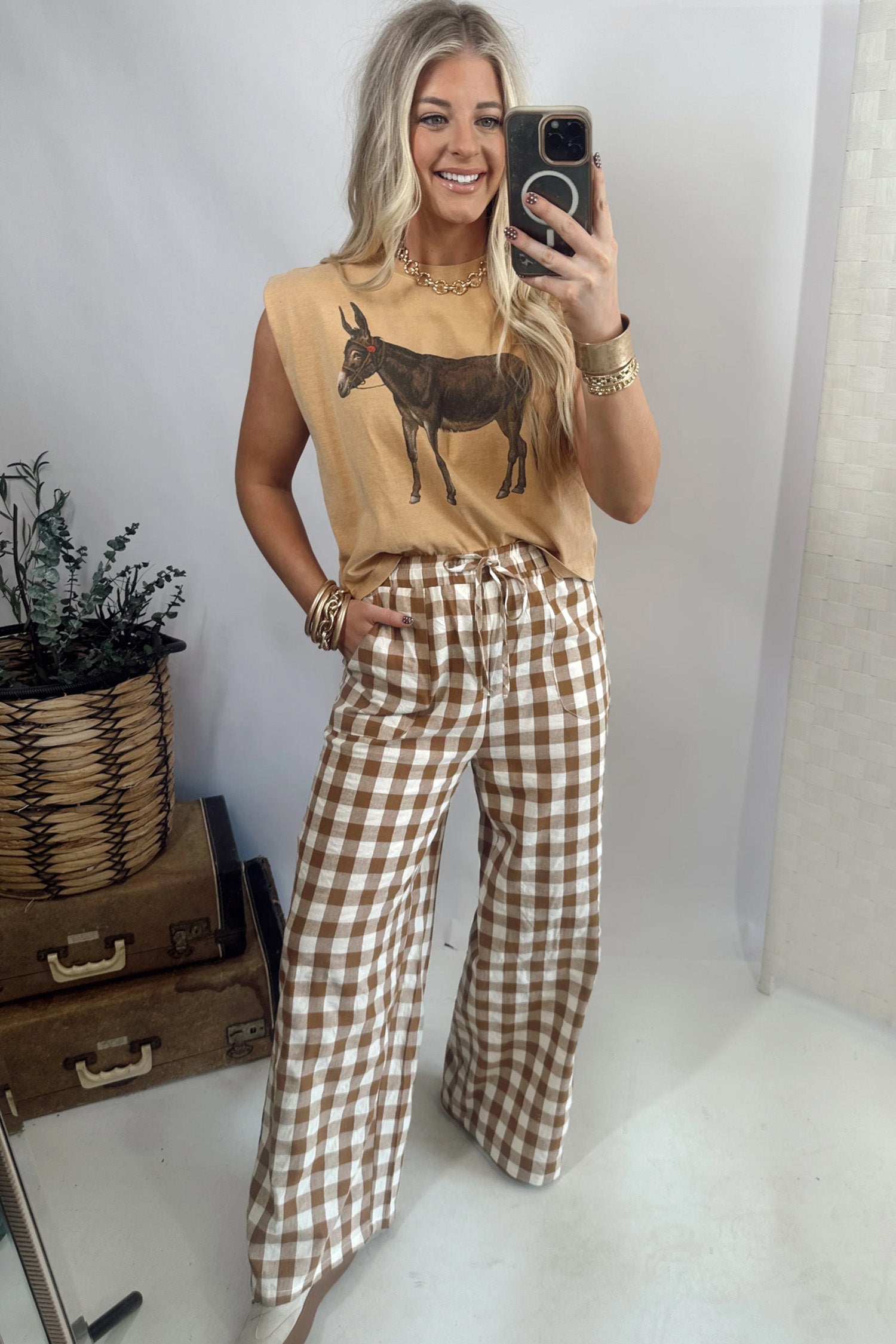 Woman taking a mirror selfie wearing a sleeveless top with a donkey graphic and checkered pants.