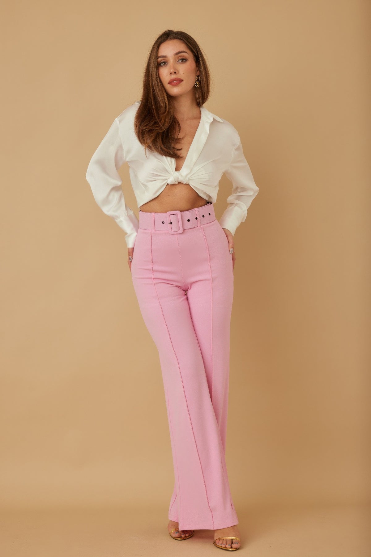 Woman wearing a white blouse and blush pink pants against a beige background