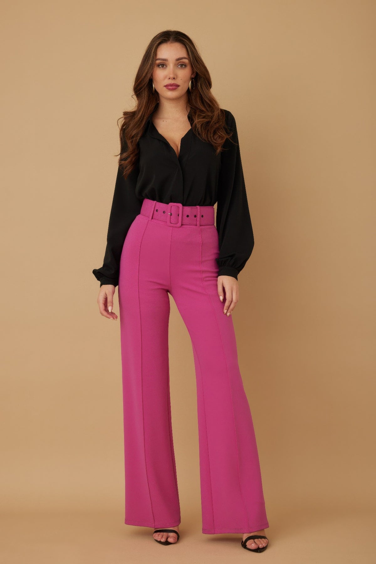 Woman wearing a black blouse and fuchsia pink pants against a beige background