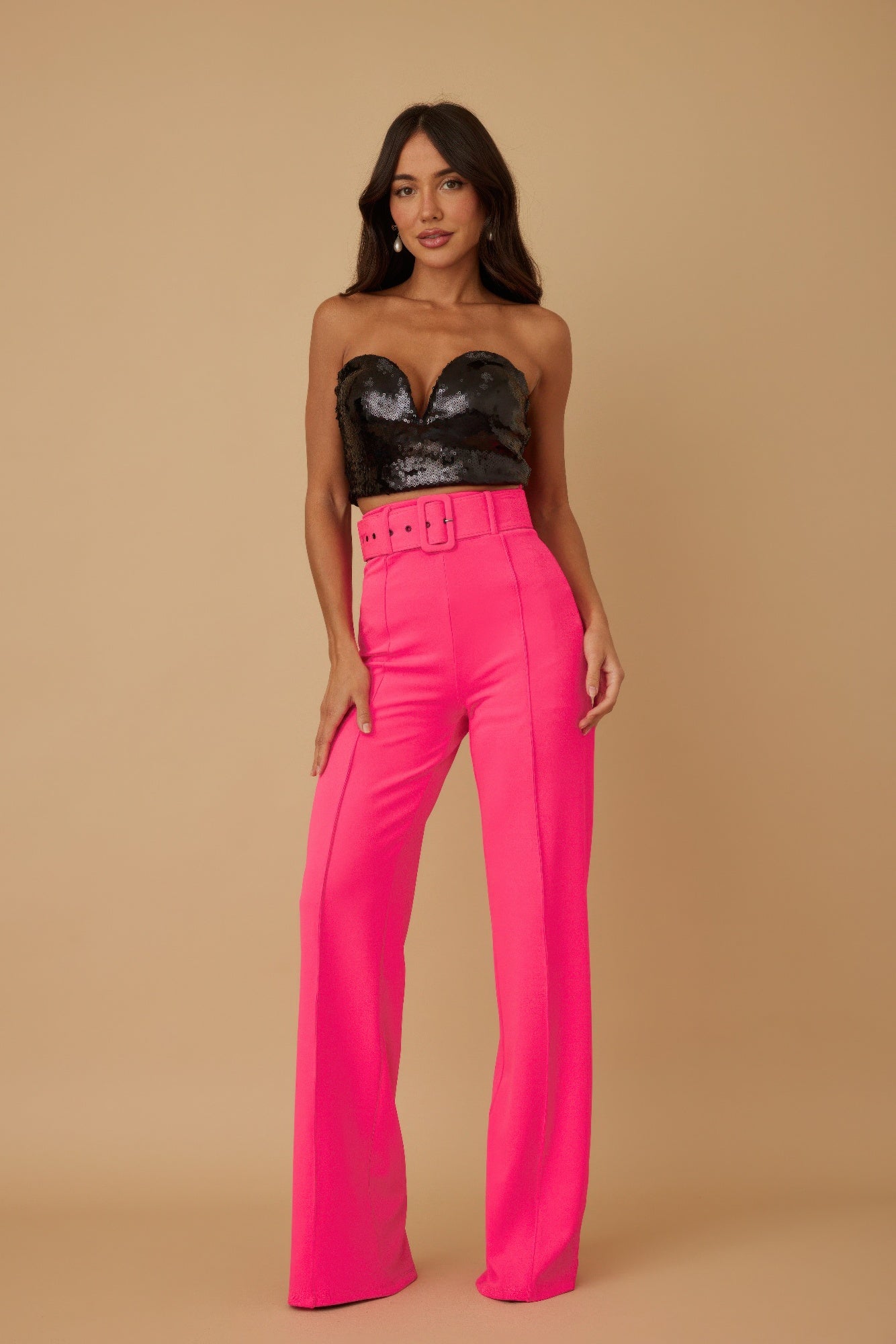 Woman wearing a black sequin top and bright pink pants against a beige background