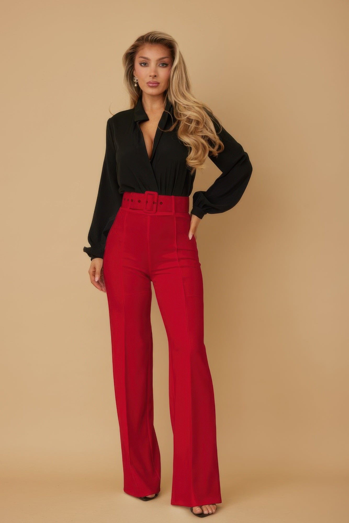 Woman wearing a black blouse and red pants against a beige background