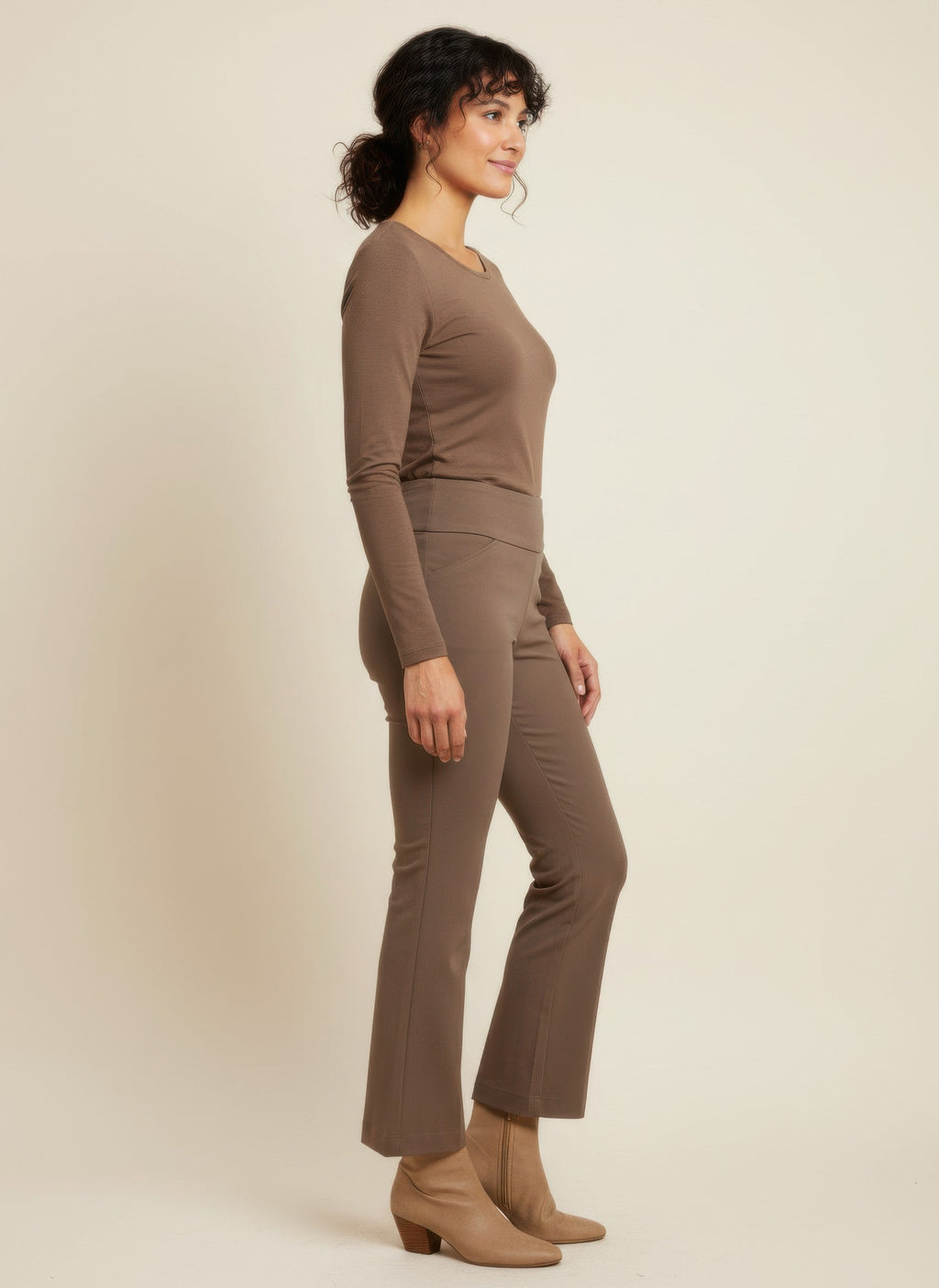 Woman wearing a brown long-sleeve top and pants on a beige background side view