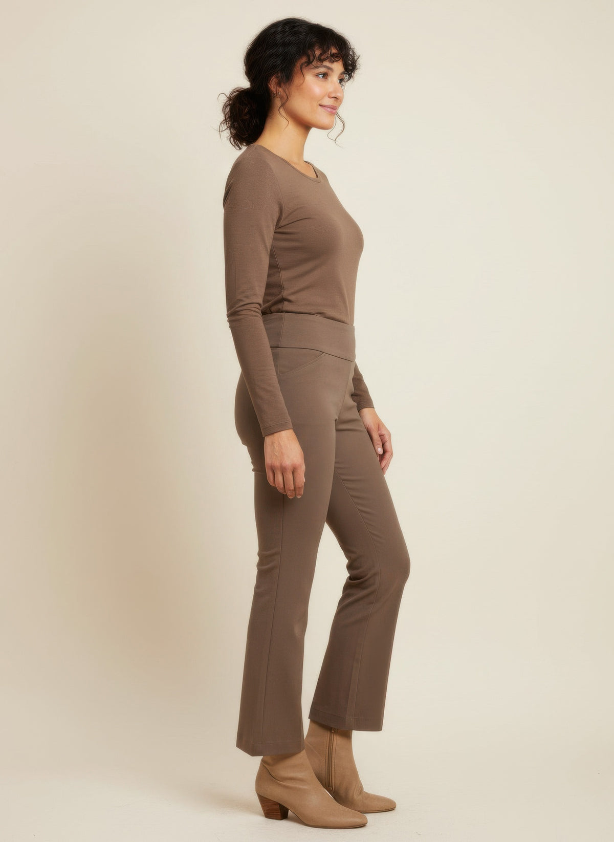 Woman wearing a brown long-sleeve top and pants on a beige background side view