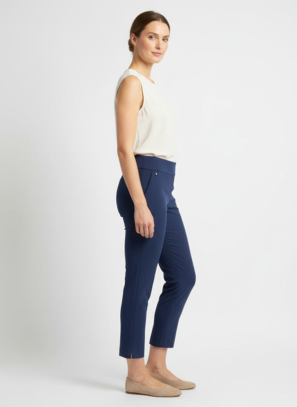 Woman wearing navy blue pants and a white top on a white background side view