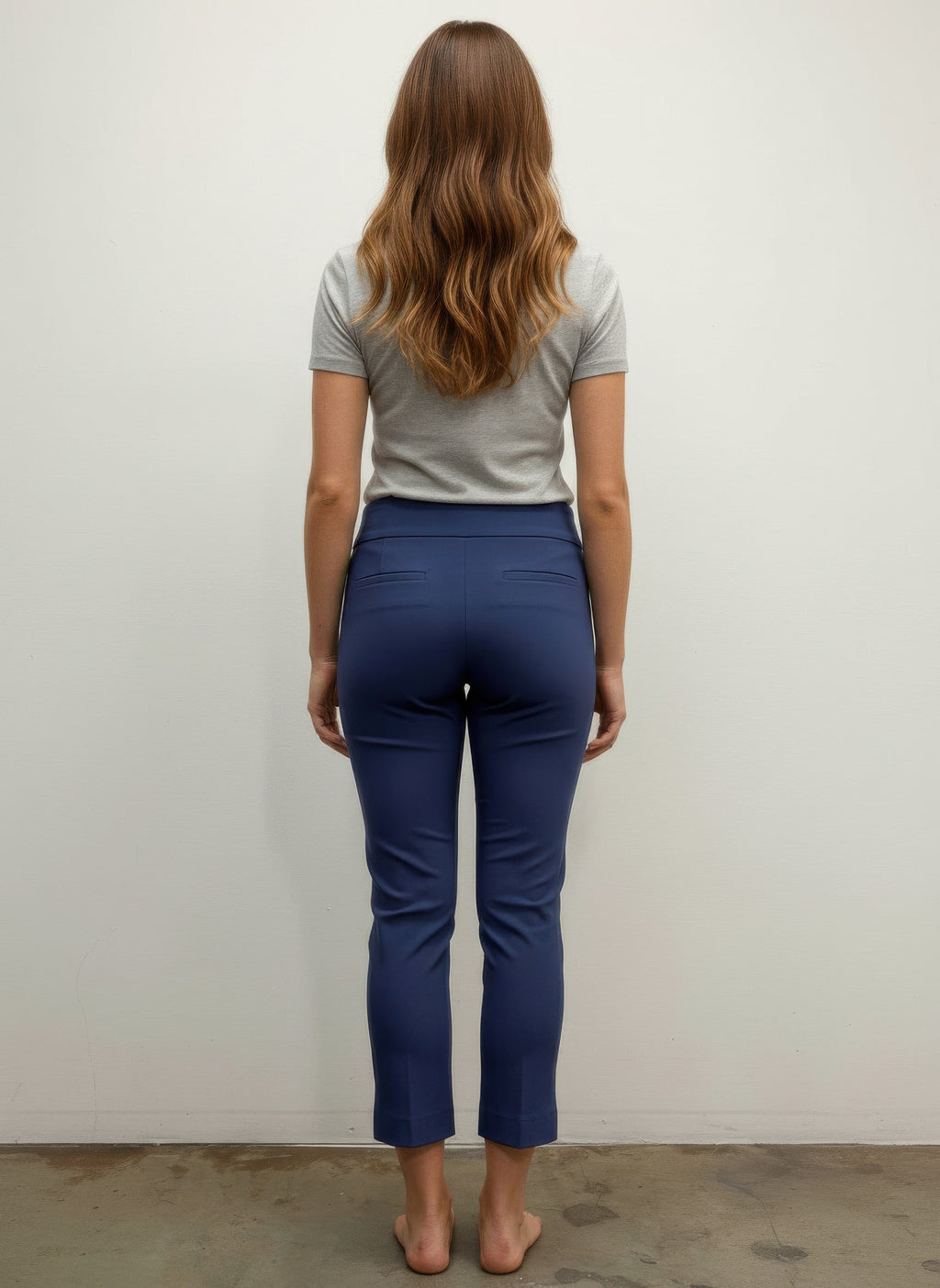 Person wearing a gray shirt and blue pants standing against a white wall. Back view