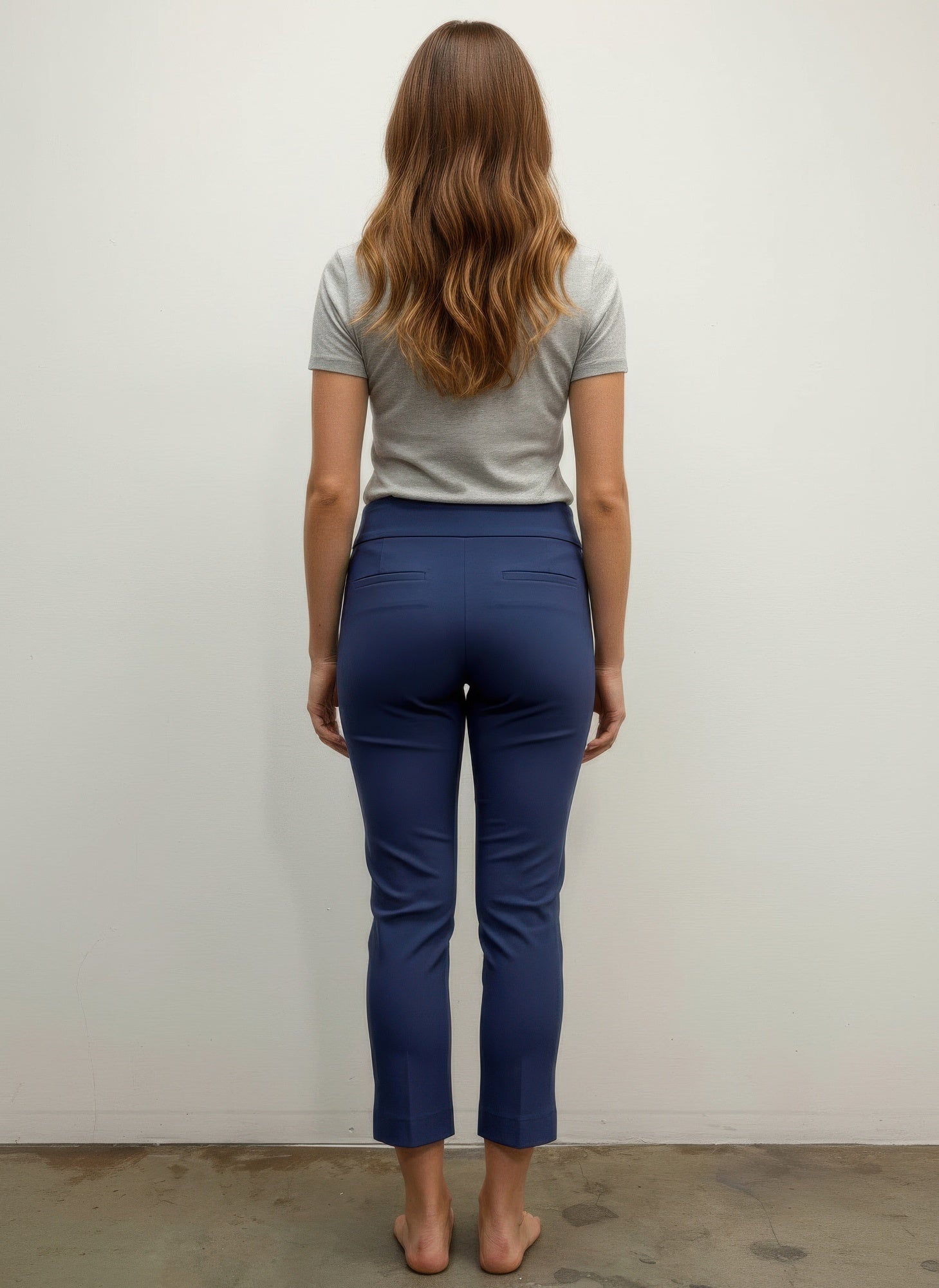 Person wearing a gray shirt and blue pants standing against a white wall. Back view