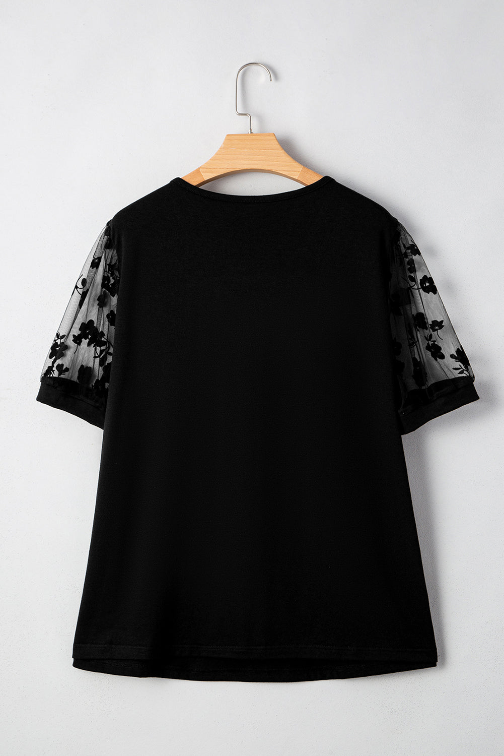 Black t-shirt with sheer sleeves on a wooden hanger against a white background