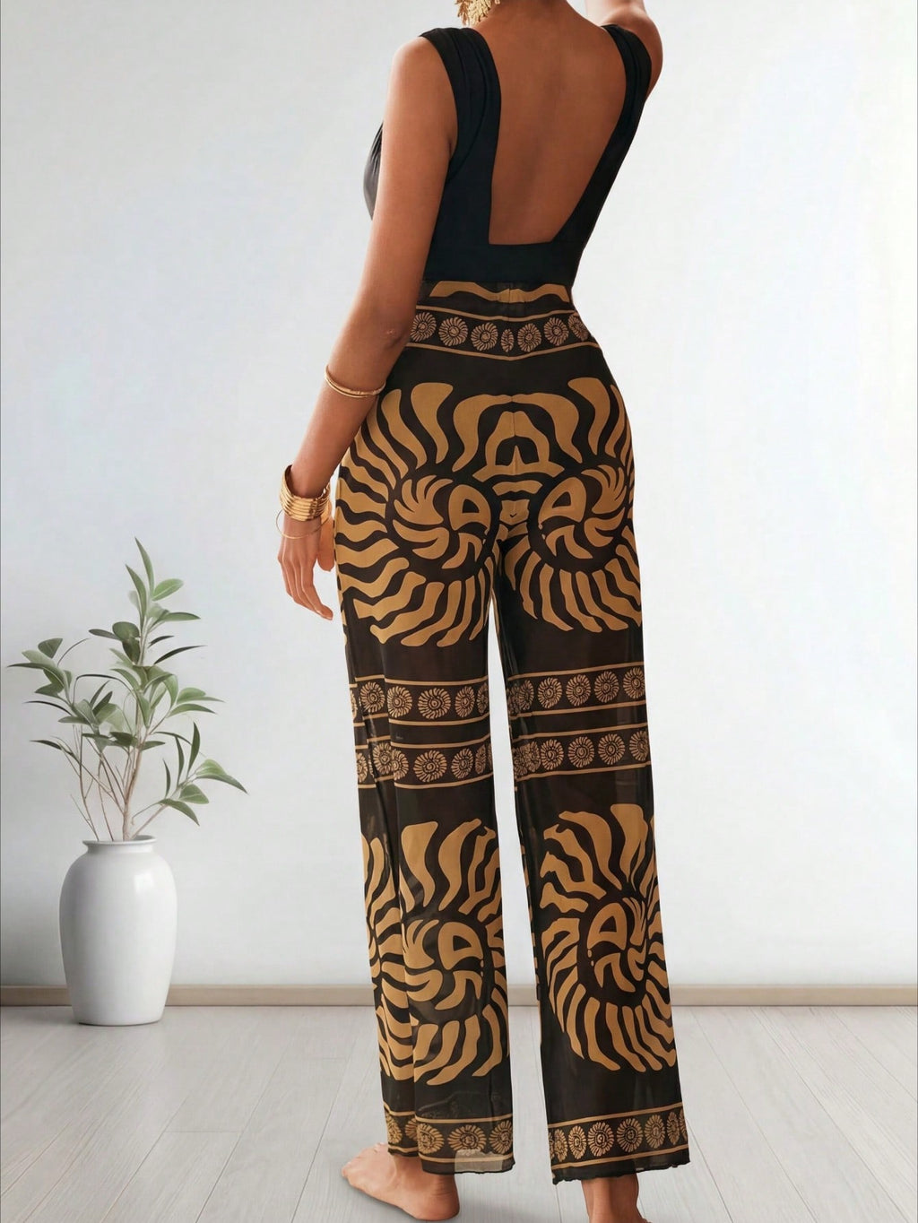 Person wearing a black and gold patterned jumpsuit in a minimal indoor setting. Back view
