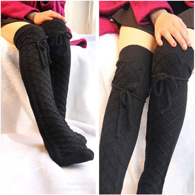 Black knitted knee-high socks with bow details worn by a person on a white background