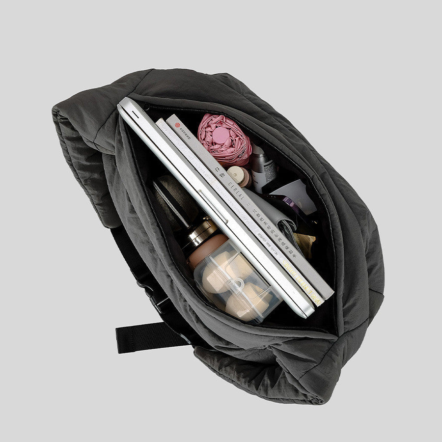 Gray backpack with items including a laptop, bottles, and yarn on a light gray background