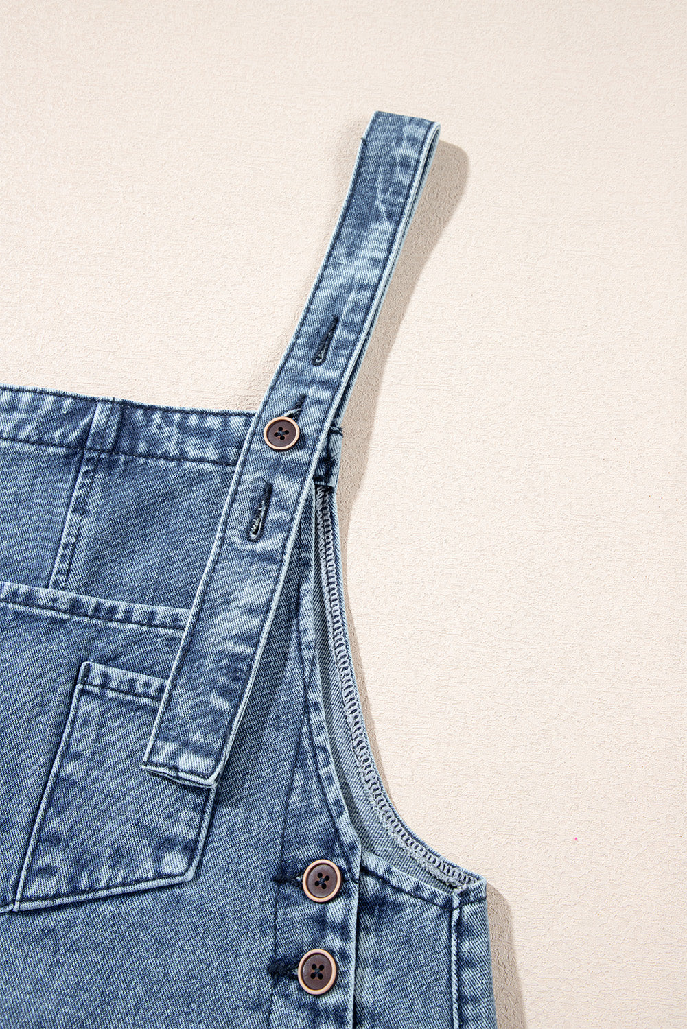 Close-up of a denim overall with buttons on a beige background