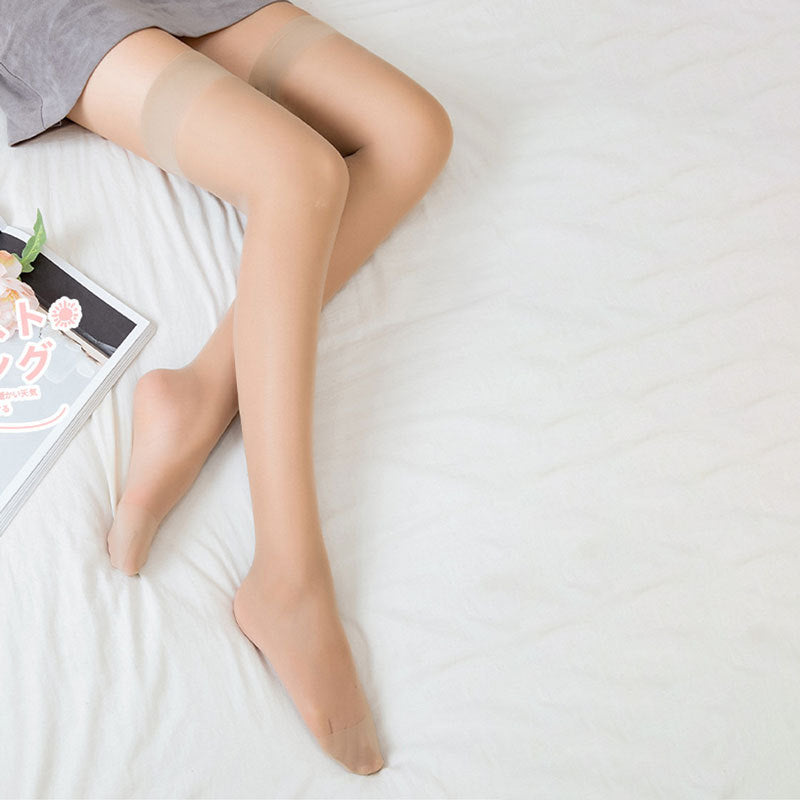 Person wearing sheer beige stockings on a white bed with a magazine.