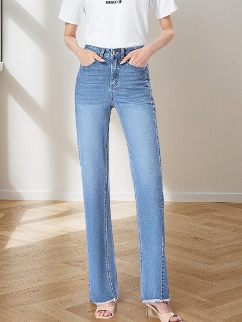 Person wearing light blue flared jeans and a white t-shirt with text, standing on a wooden floor.