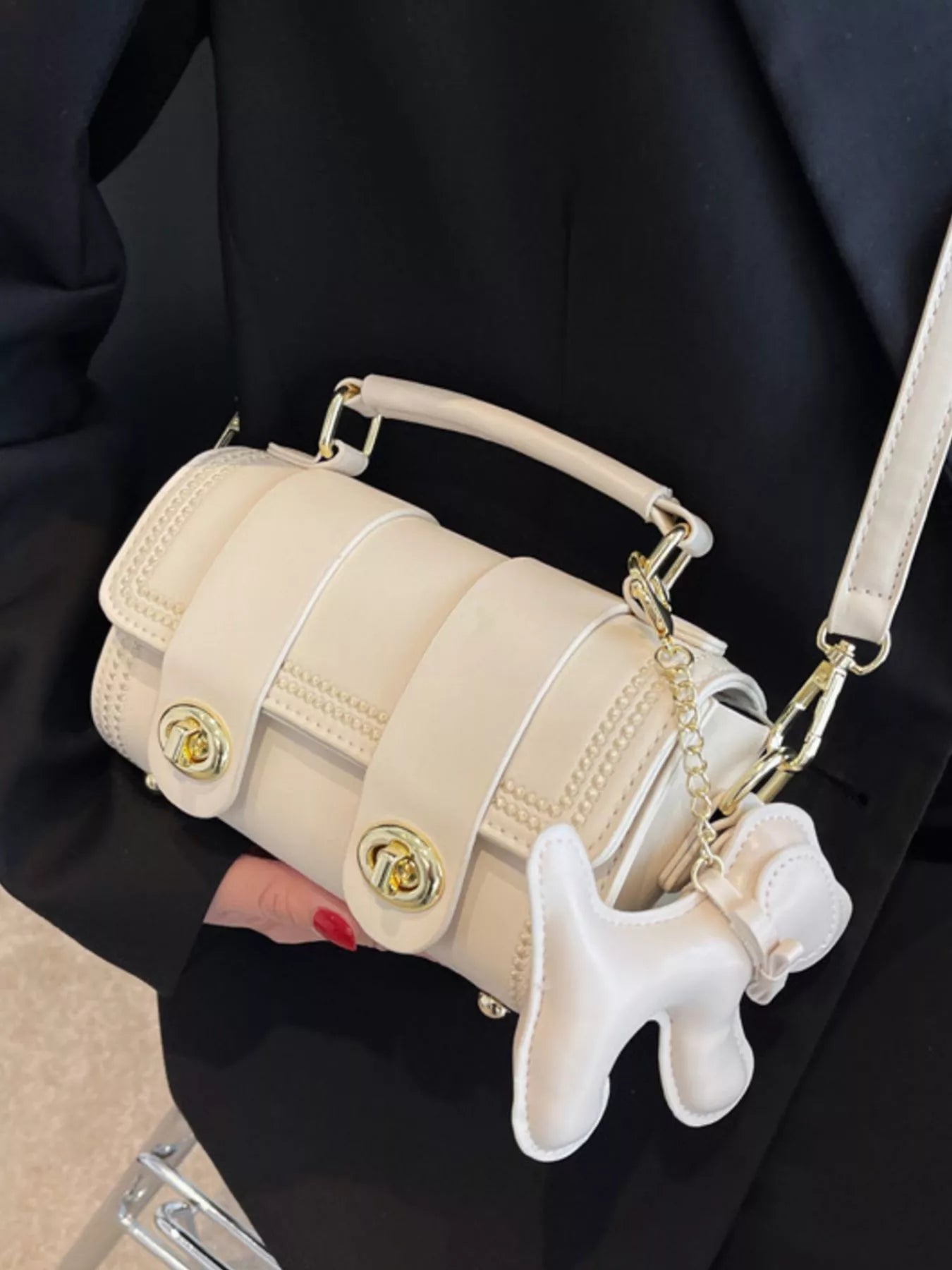 Beige handbag with a dog-shaped charm held by a person wearing a black outfit.