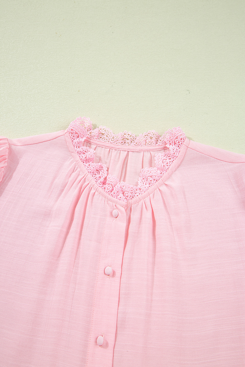 Close-up of a pink blouse with lace trim on a light green background