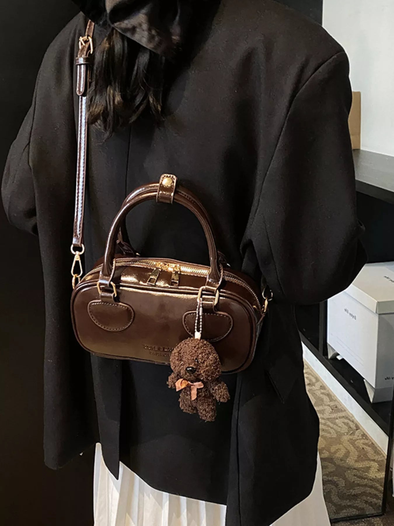 Person wearing a black coat with a brown handbag featuring a teddy bear charm.
