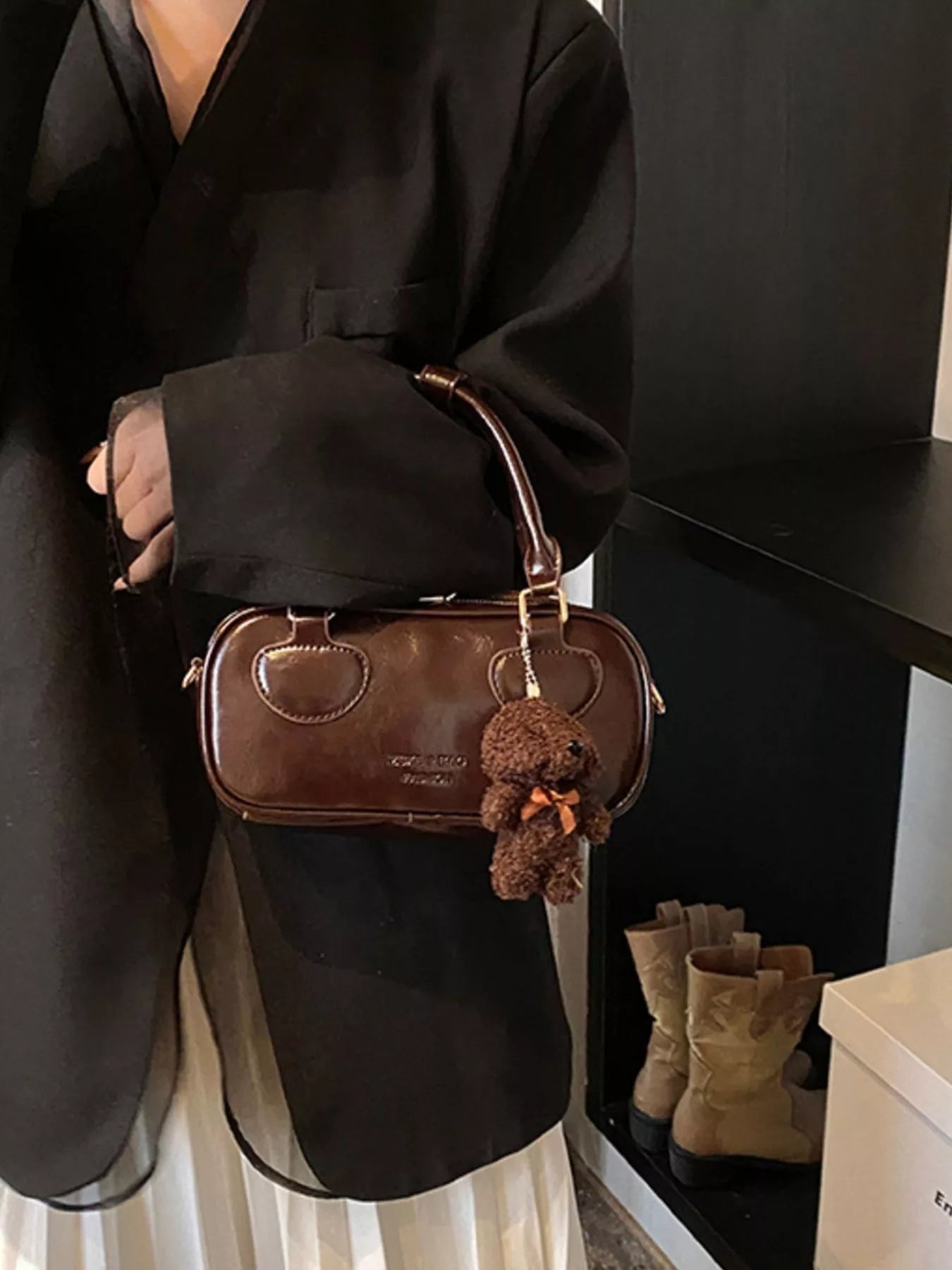Person holding a brown handbag with a keychain, wearing a black outfit.