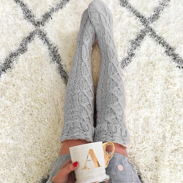 Person wearing gray patterned tights holding a white mug with gold letter 'A' on a white rug with black diamond pattern.