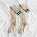 Pair of beige knee-high socks with green stripes on a white fabric background