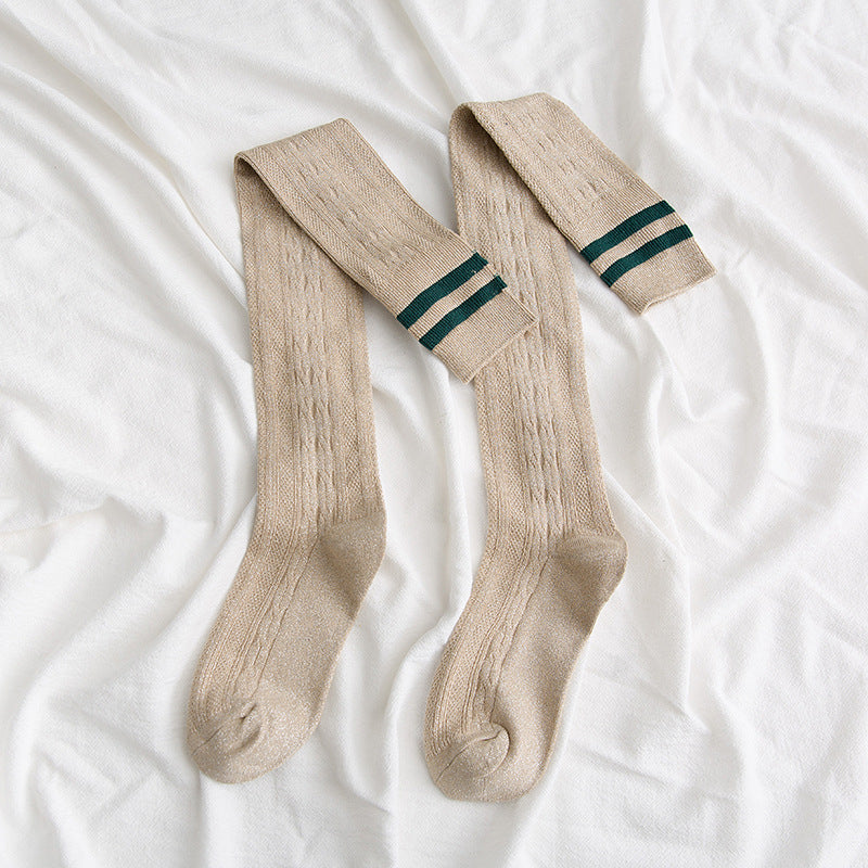 Pair of beige knee-high socks with green stripes on a white fabric background