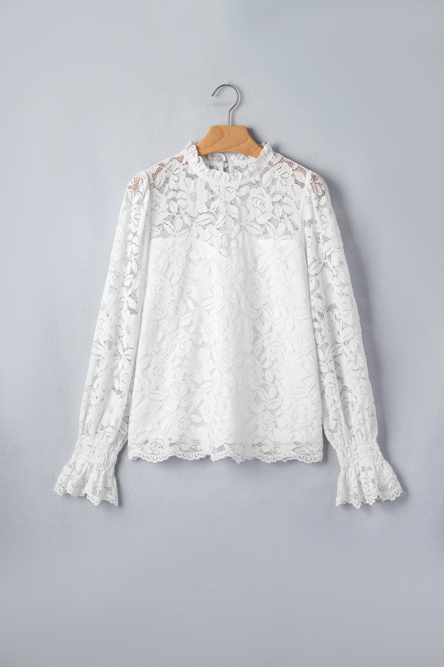 White lace blouse on a wooden hanger against a gray background