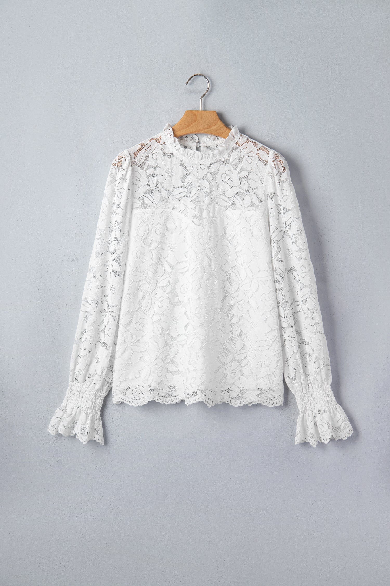 White lace blouse on a wooden hanger against a gray background