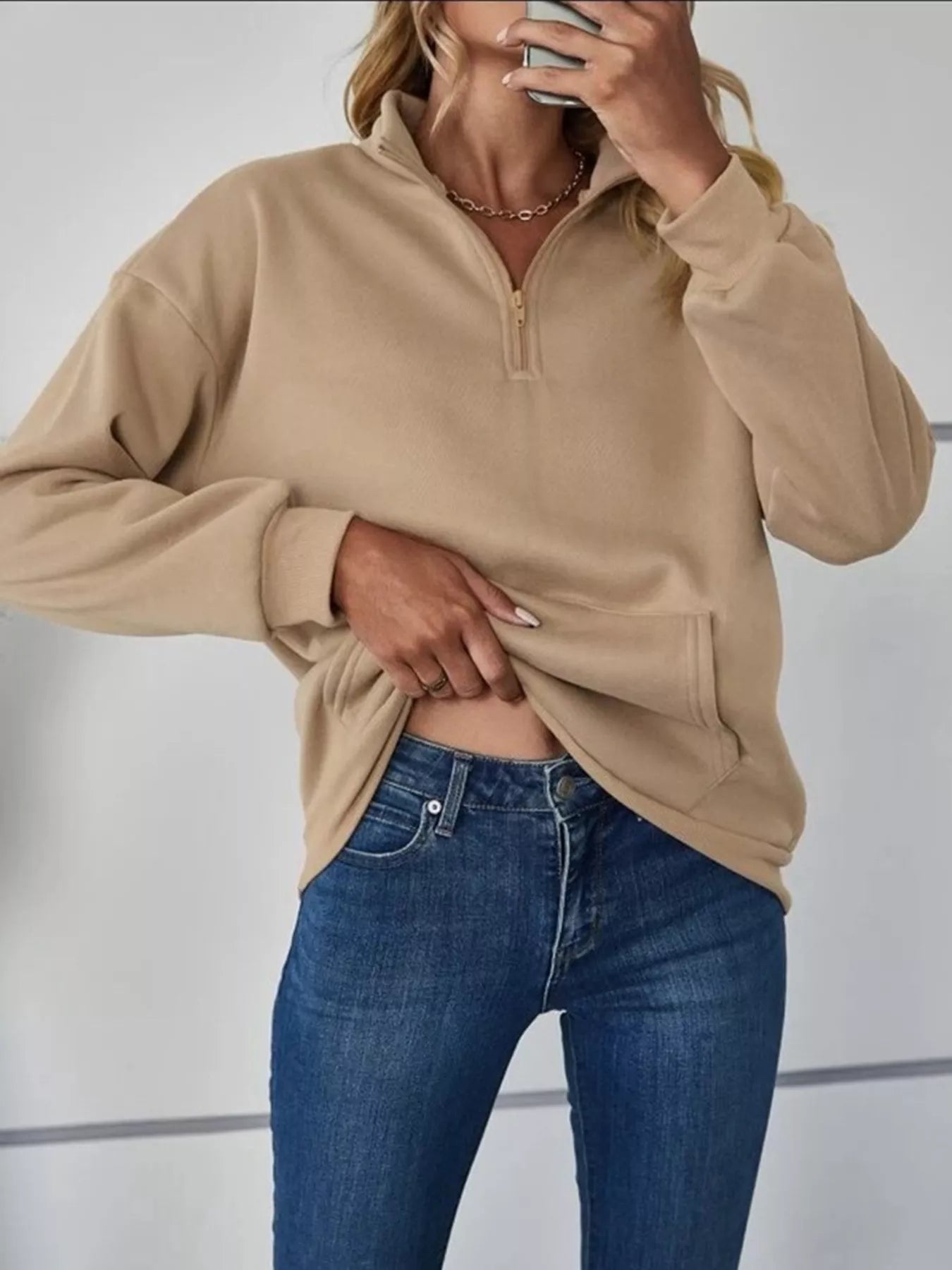 Person wearing a beige pullover and blue jeans against a neutral background