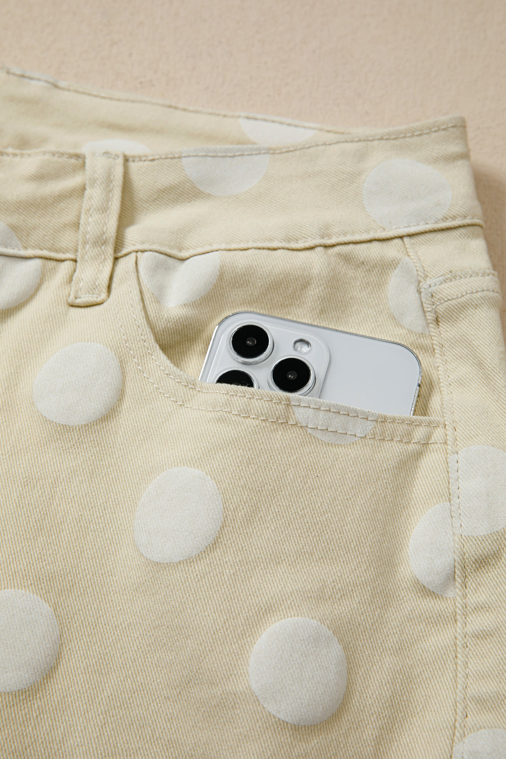 Phone in a pocket of polka dot pants on a beige background pocket view