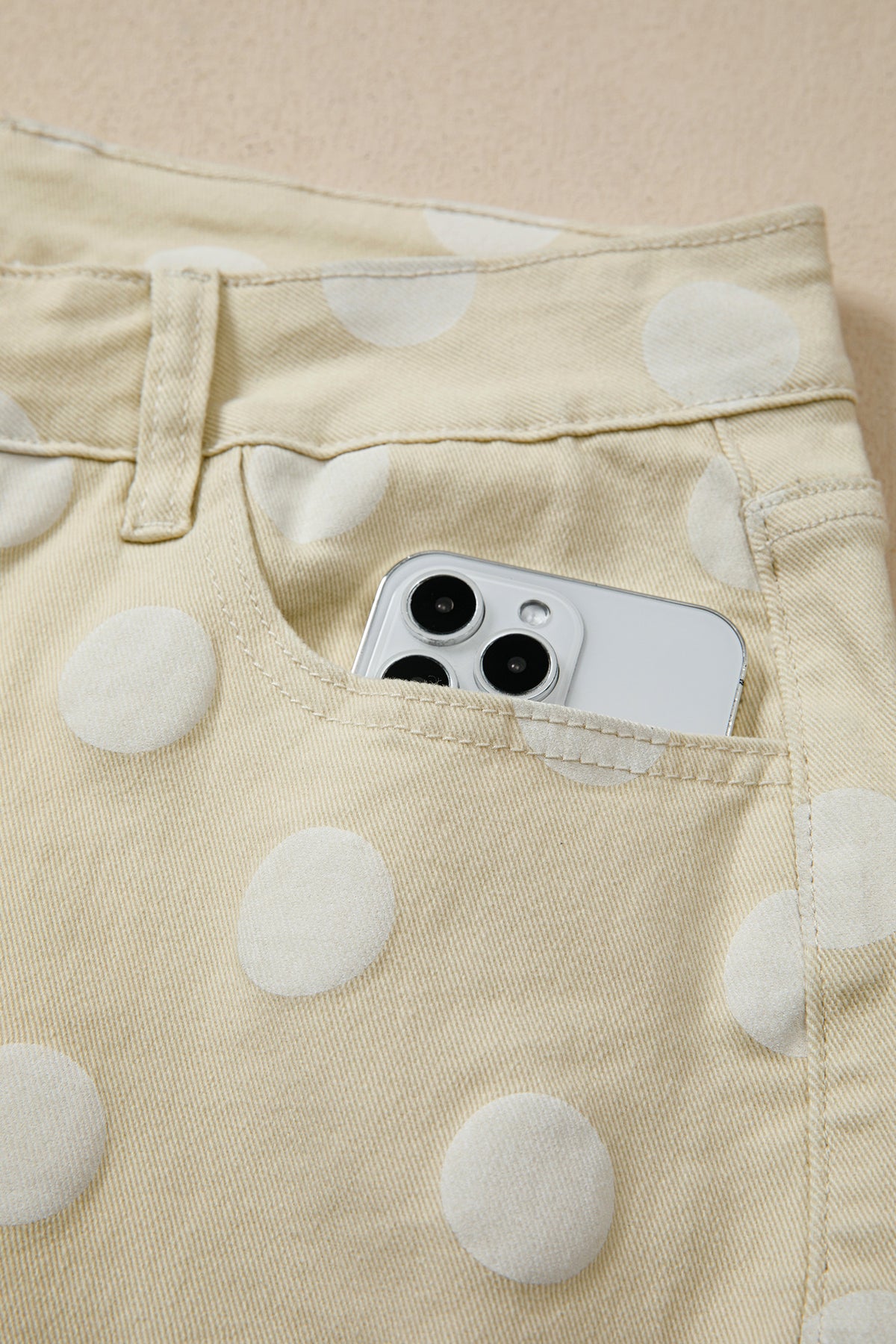 Phone in a pocket of polka dot pants on a beige background pocket view