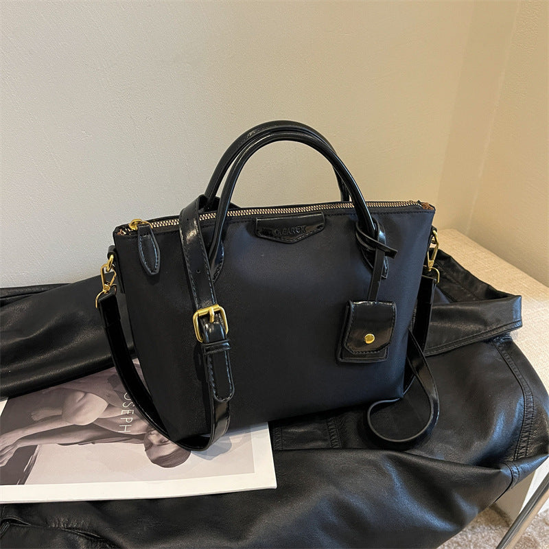 Black handbag on a black leather surface with a magazine underneath