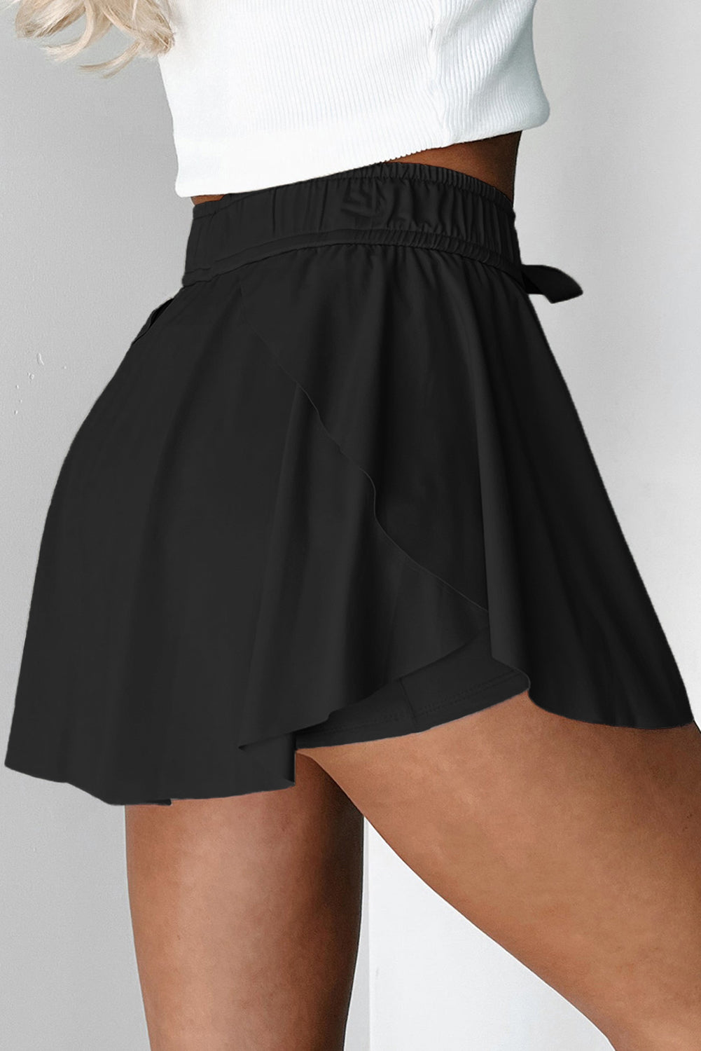 Black tennis shorts worn by a person on a plain background side view