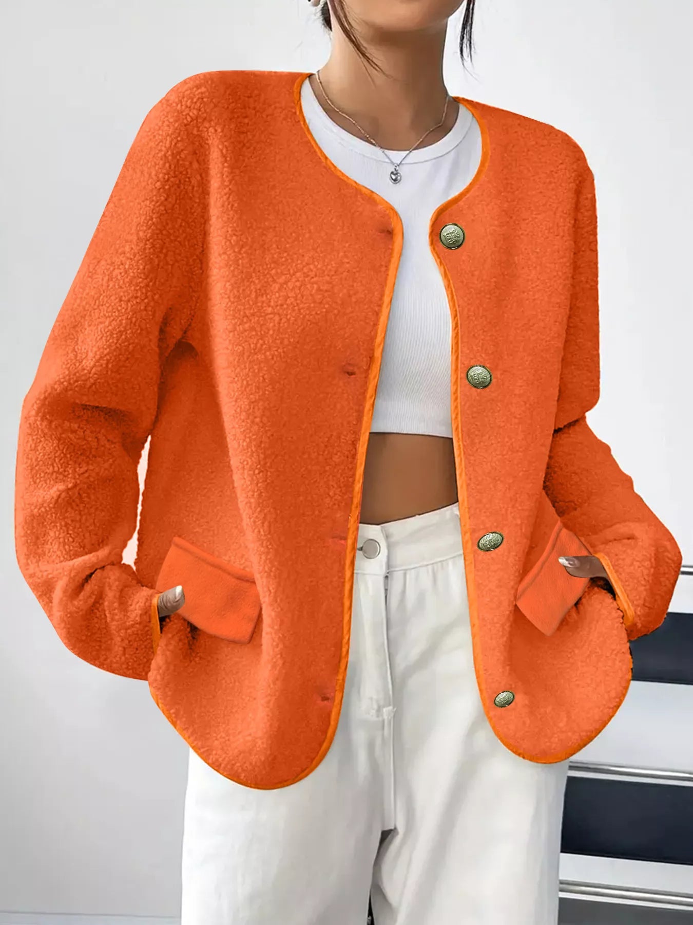 Person wearing an orange cardigan over a white top and pants on a plain background