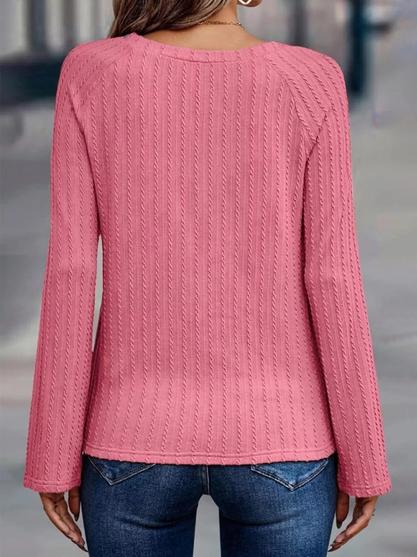 Pink cable knit sweater worn by a person on a blurred street background