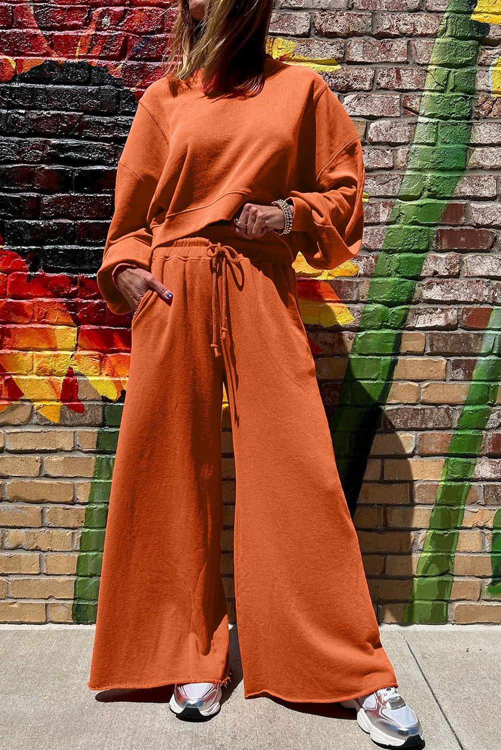 Person wearing an orange outfit standing in front of a colorful brick wall.