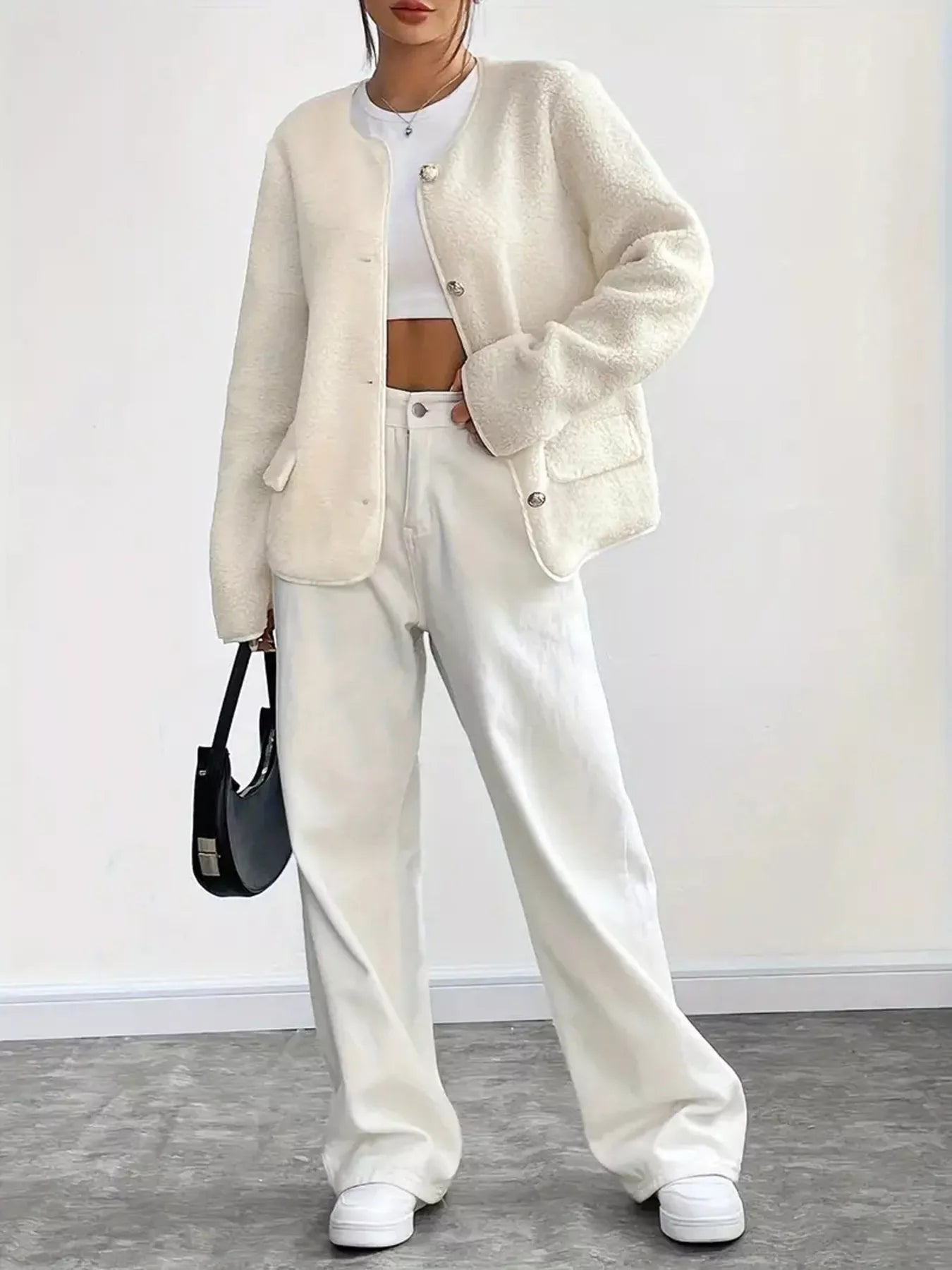 Person wearing a cream cardigan, white pants, and white sneakers against a plain background