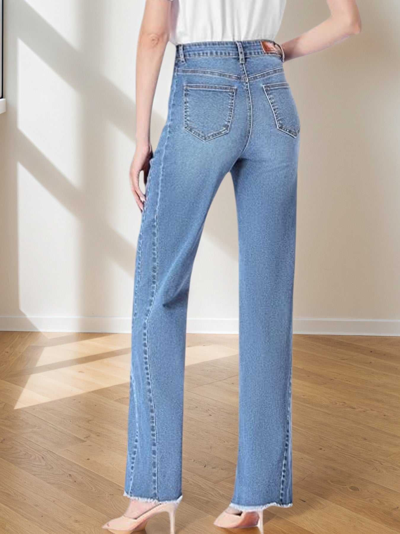 Person wearing light blue jeans in a room with wooden floor and white wall