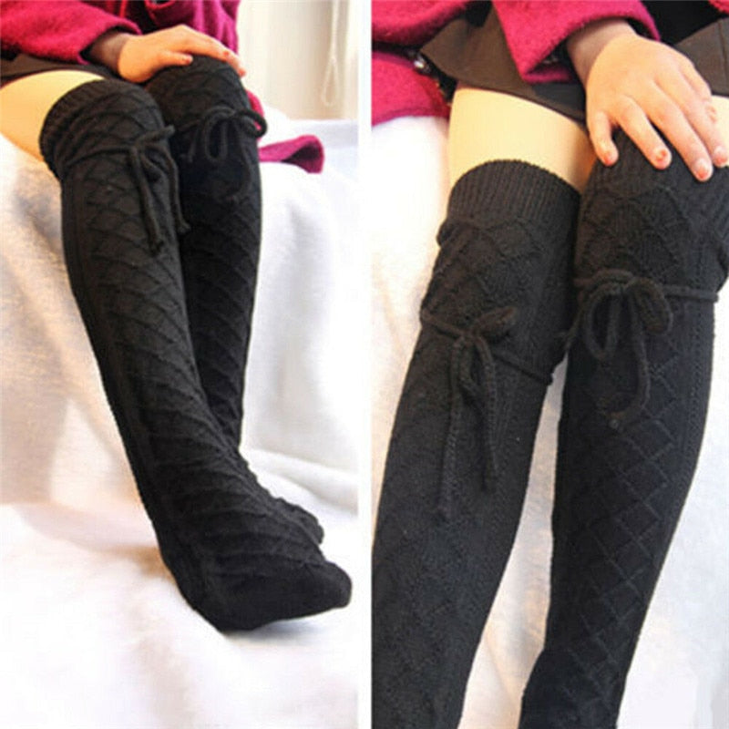Black knitted knee-high socks with bow details worn by a person on a white background