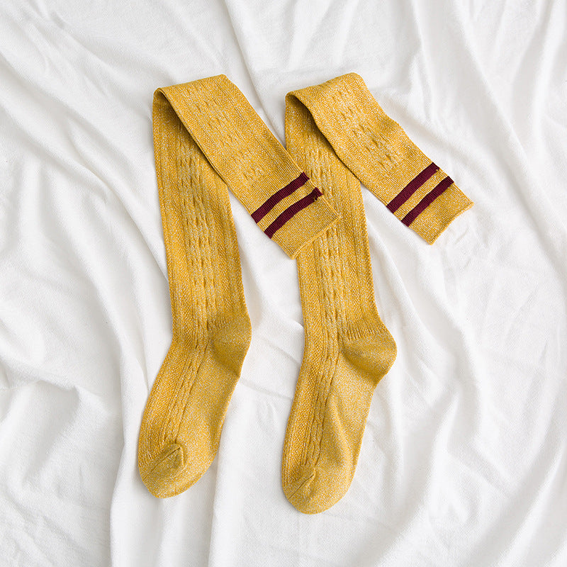 Pair of mustard yellow socks with red stripes on a white fabric background