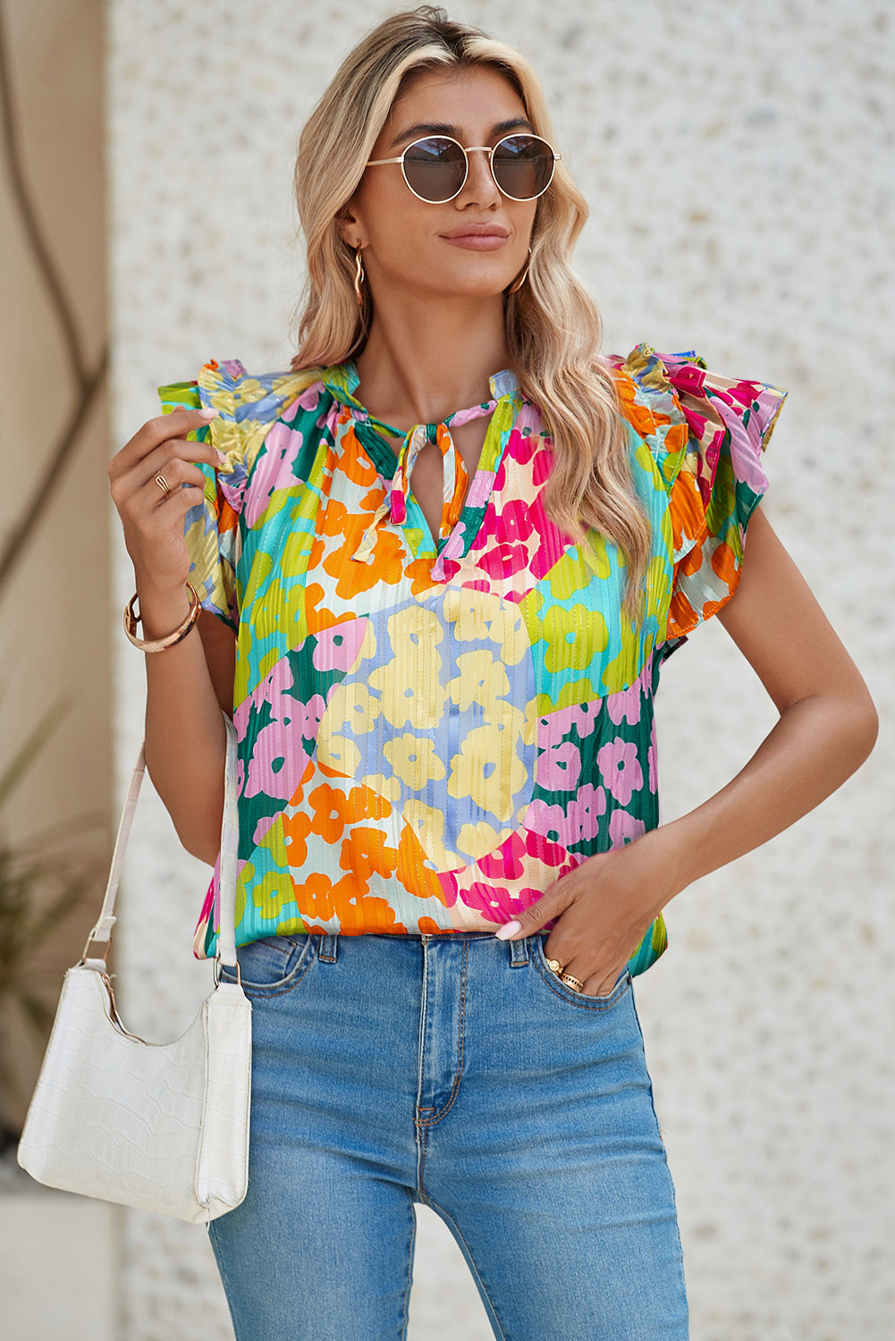 Woman wearing a colorful floral top and blue jeans against a neutral background