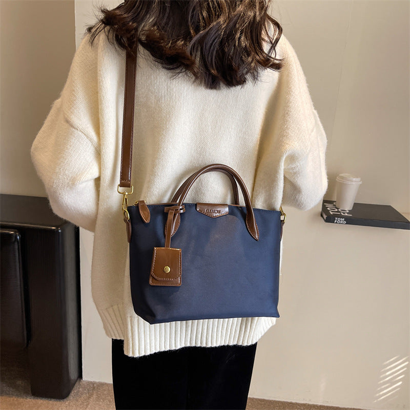 Person wearing a white sweater with a blue handbag featuring brown leather accents.