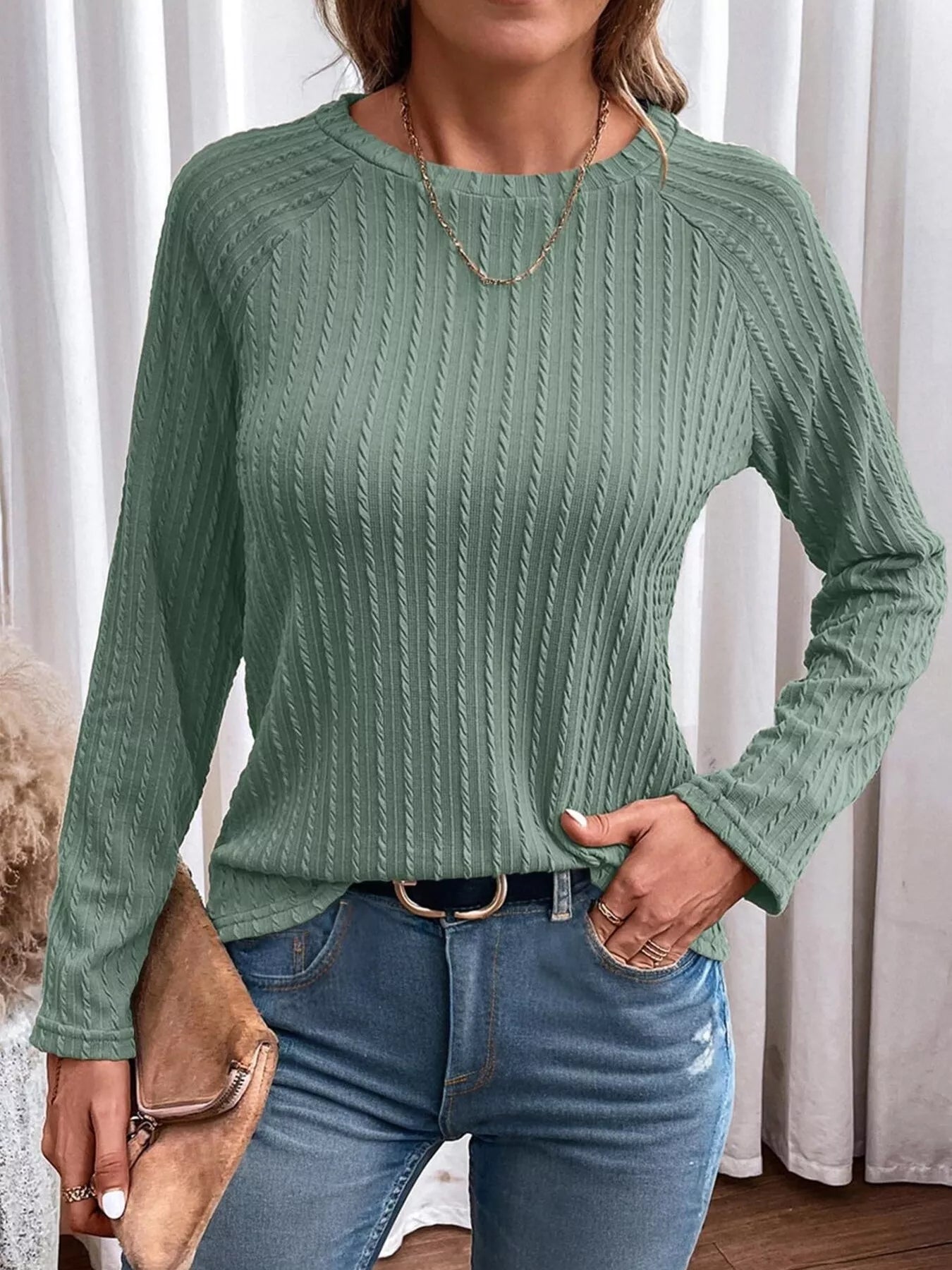 Person wearing a green ribbed sweater and blue jeans with a neutral background
