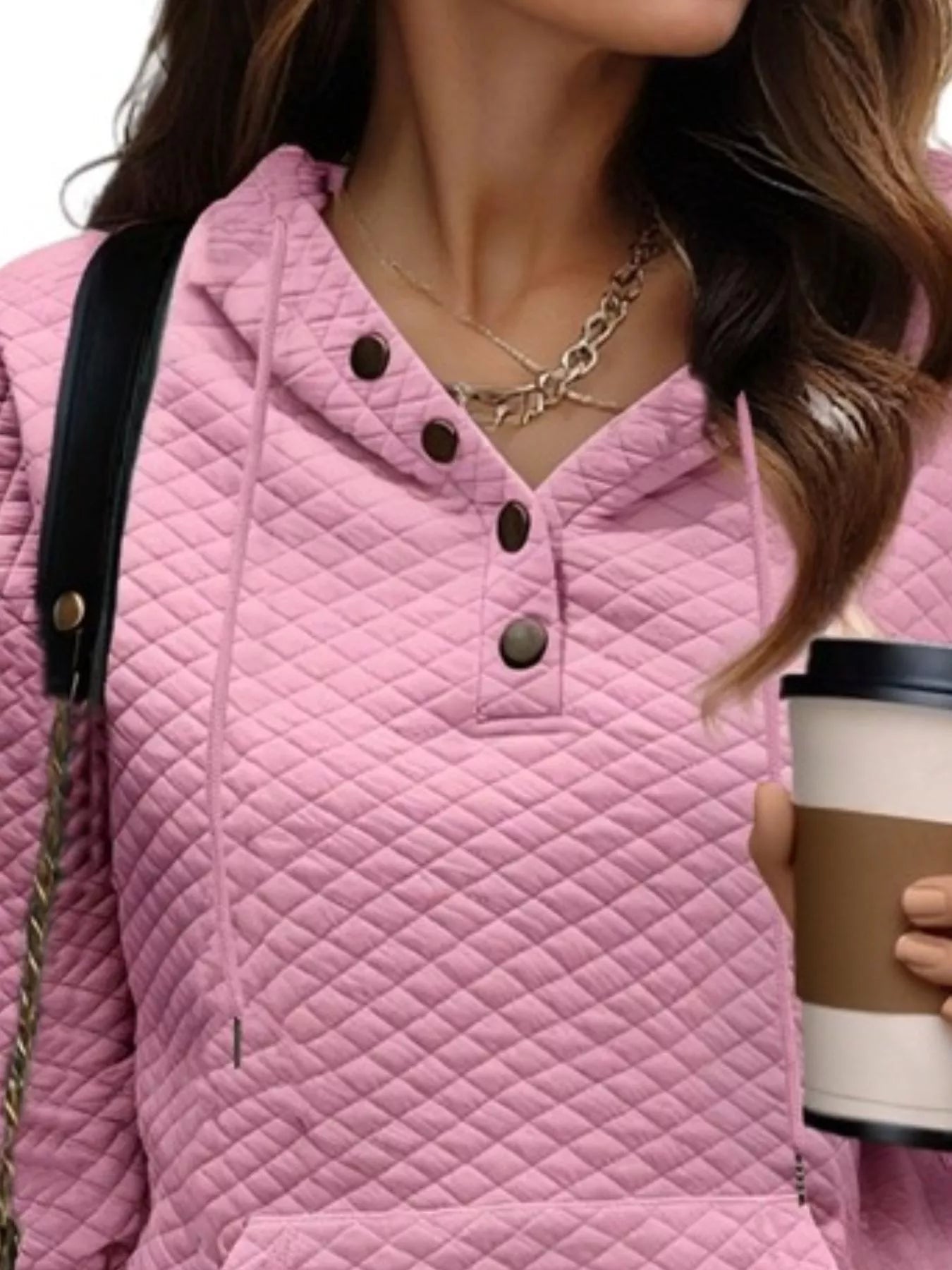 Person wearing a pink quilted jacket holding a coffee cup.