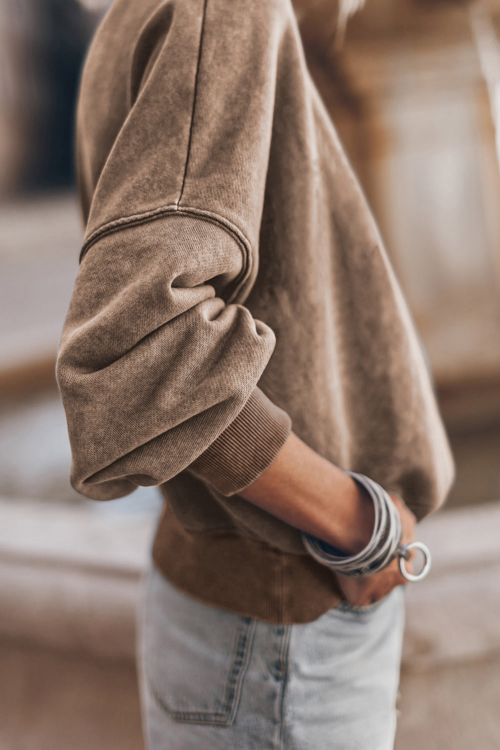 Close-up of a person wearing a brown sweater and light blue jeans with a blurred background
